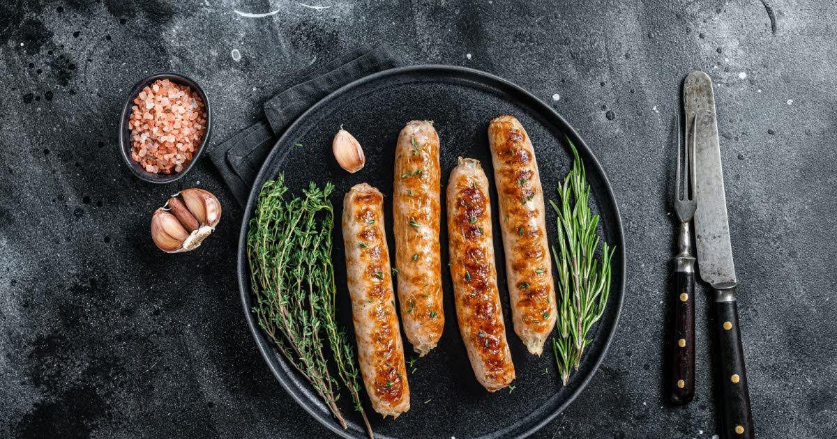 Grilled sausages on a black plate, garnished with herbs and garlic, showcasing Creative Vienna Sausages Treats.