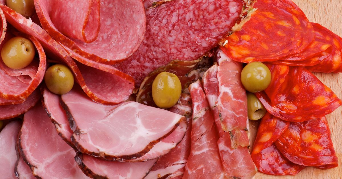 A cutting board displaying an assortment of processed meats, including pepperoni and sausage, alongside various olives.
